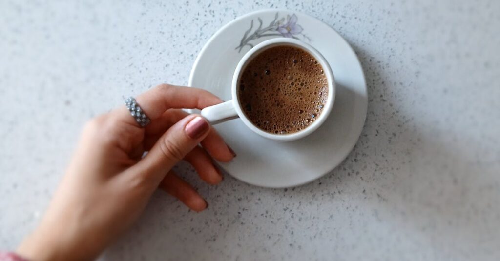 A close-up of a hand holding a cup of coffee on a white table, showcasing relaxation and simplicity.